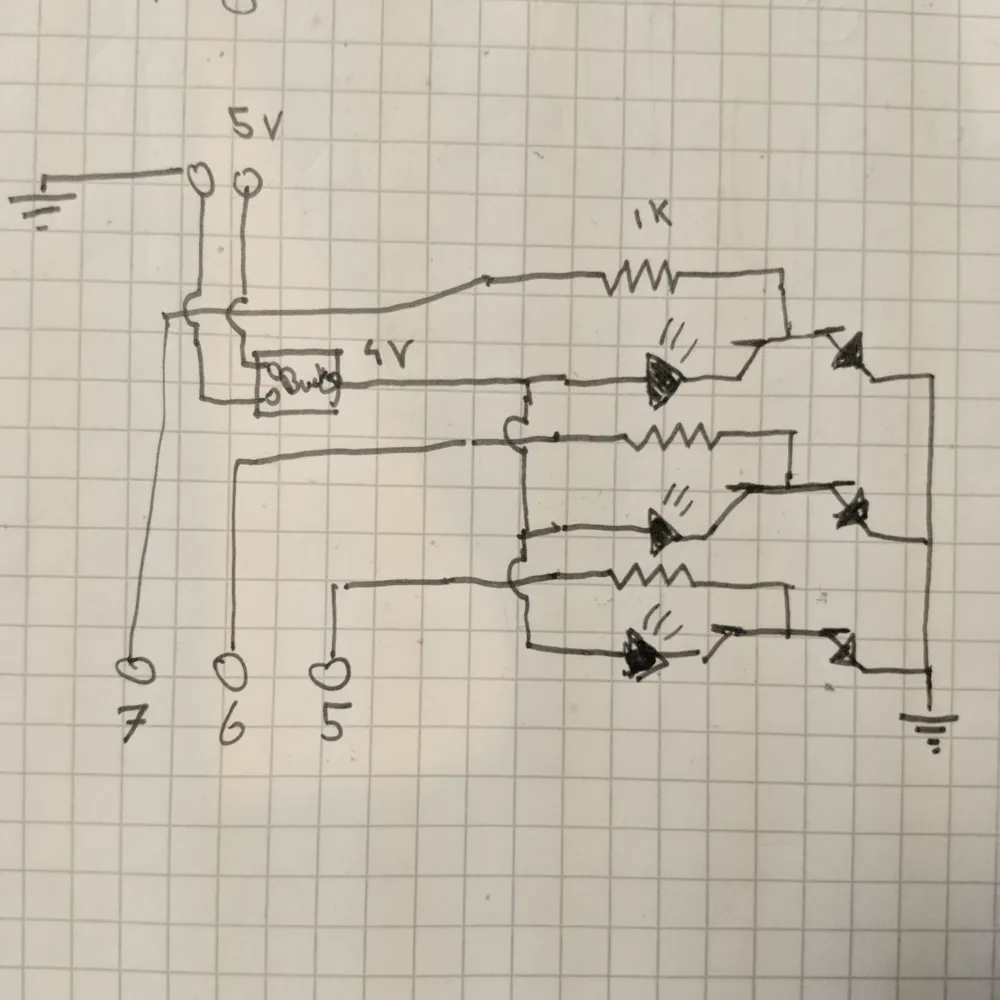 The circuit plan Hand-drawn schematic on grid paper: three LEDs switched by transistors with 1k base resistors on GPIO 5, 6 and 7, powered by a buck converter from 5V