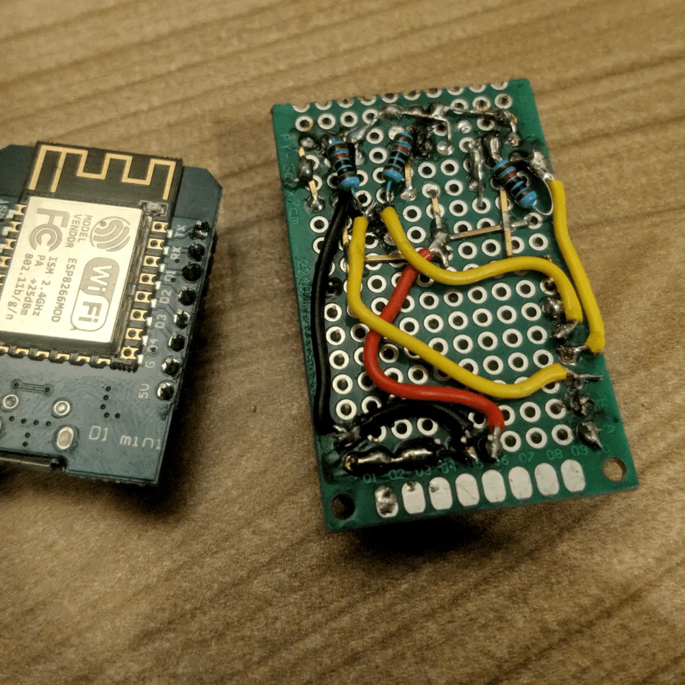 The solder side, a bit of a mess Solder side of the perfboard with resistors and yellow, red and black jumper wires, next to a Wemos D1 mini